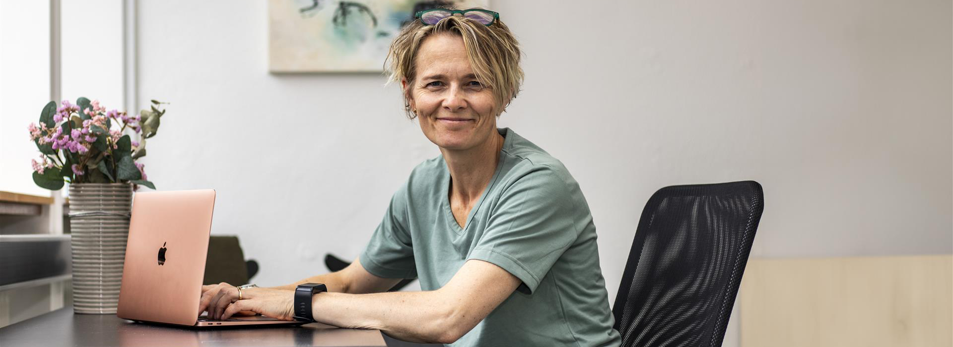 Portræt af smilende kvinde ved skrivebord med bærbar computer