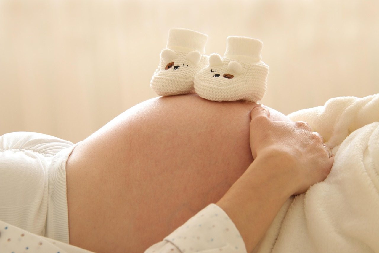 Gravid mave med små hvide babysko – et roligt og nært øjeblik, der symboliserer tryghed og nærhed i graviditeten og parforholdet. Billedet understøtter stemningen i workshoppen kærlighedsforberedelse for kommende forældre.